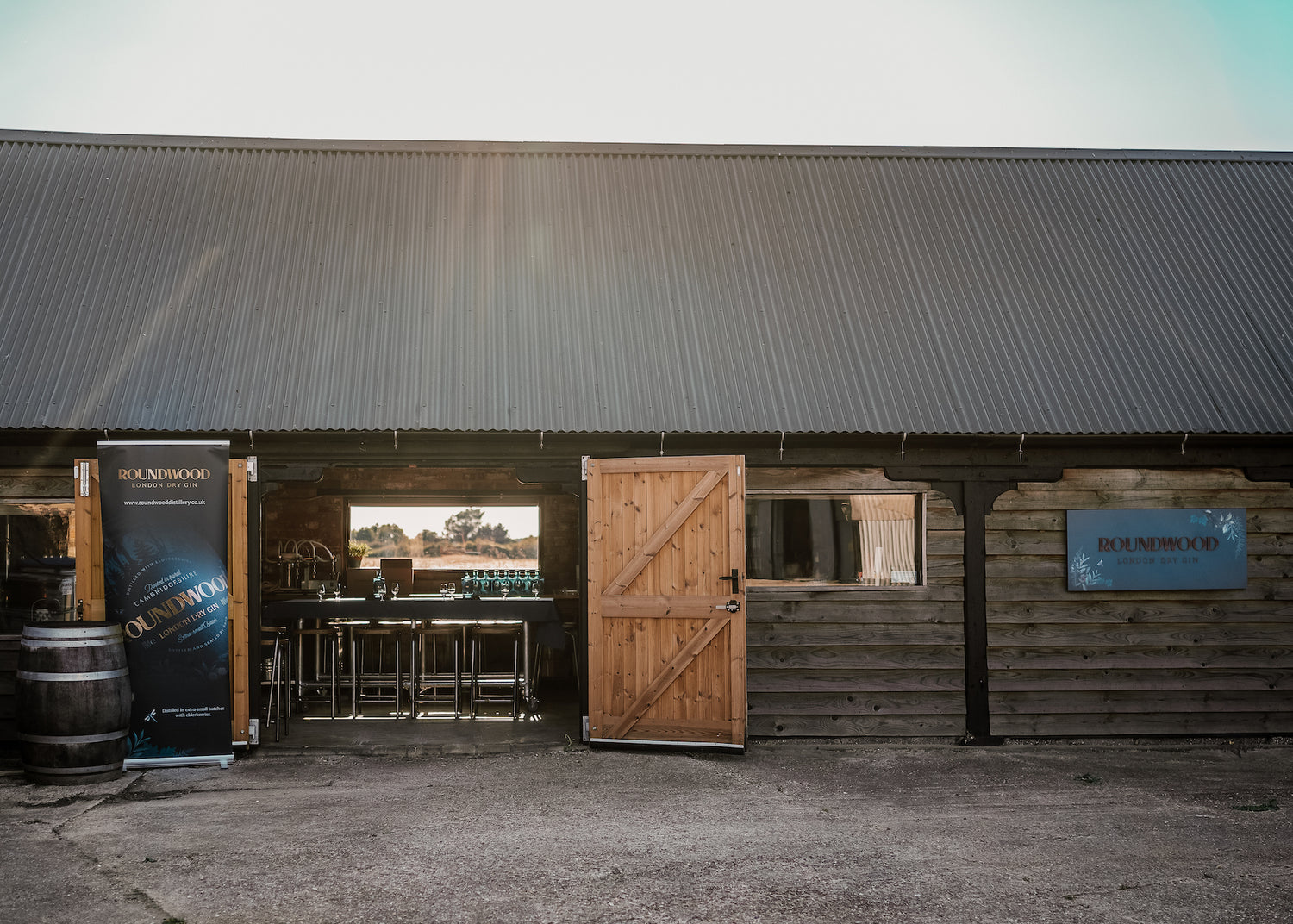 Exterior of the distillery, wooden barn with doors open wide and light shining through the window opposite across table laid for gin tasting event
